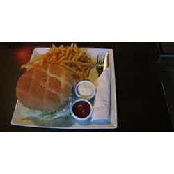 En tallerken med en burger, pommes frites, ketchup og mayonnaise ved siden af en sammenrullet serviet med gaffel og kniv på et mørkt bord.